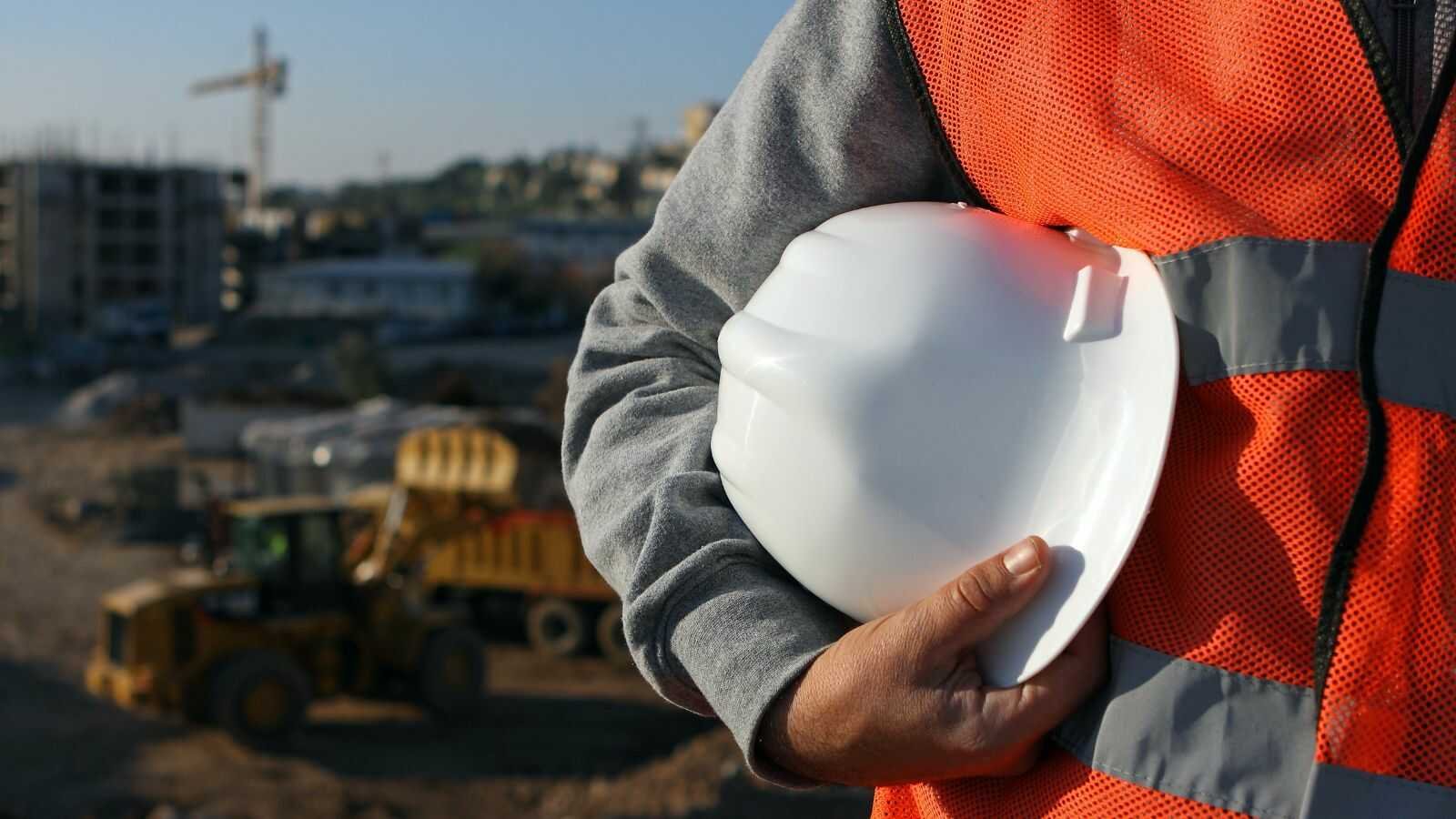 Aannemer en architect bekijken bouwplannen op werf met dakconstructie in aanbouw
